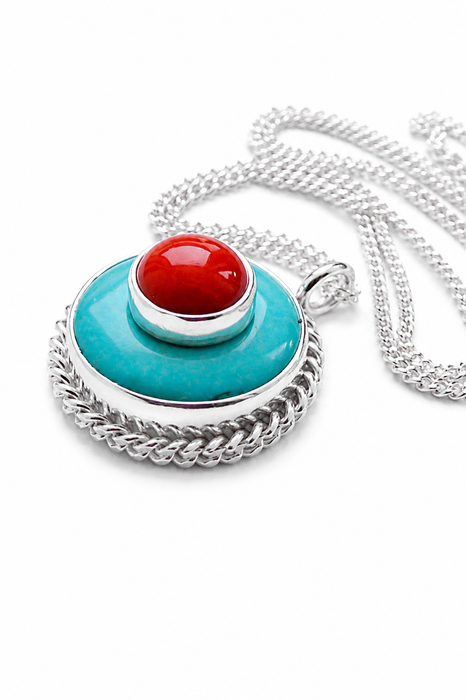 A silver pendant necklace featuring a round turquoise blue turquoise disc with a braided silver border, topped with a smaller silver ring holding a red coral cabochon stone, shown on a white background.